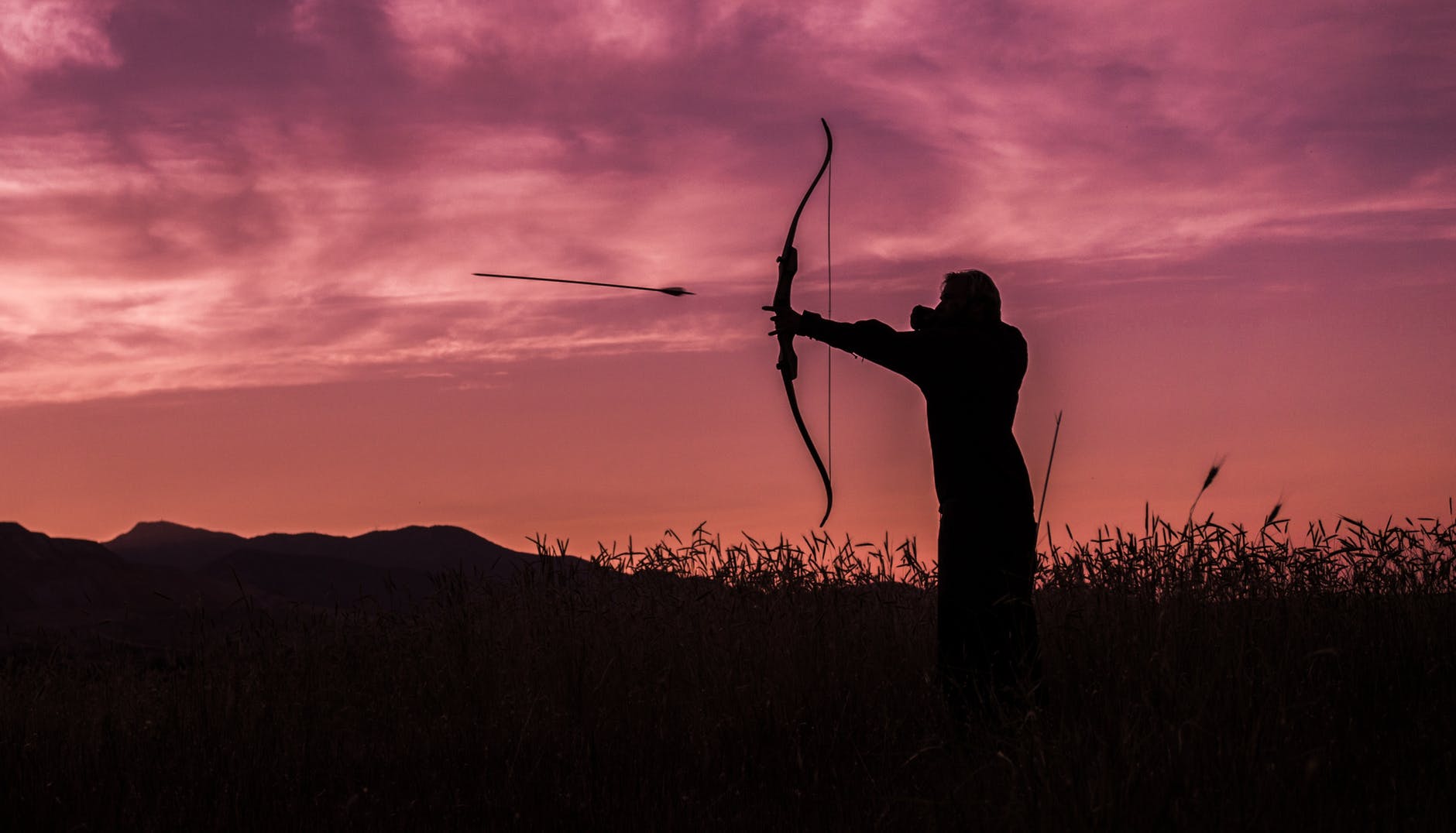 Silhouette of an archer at sunset firing an arrow